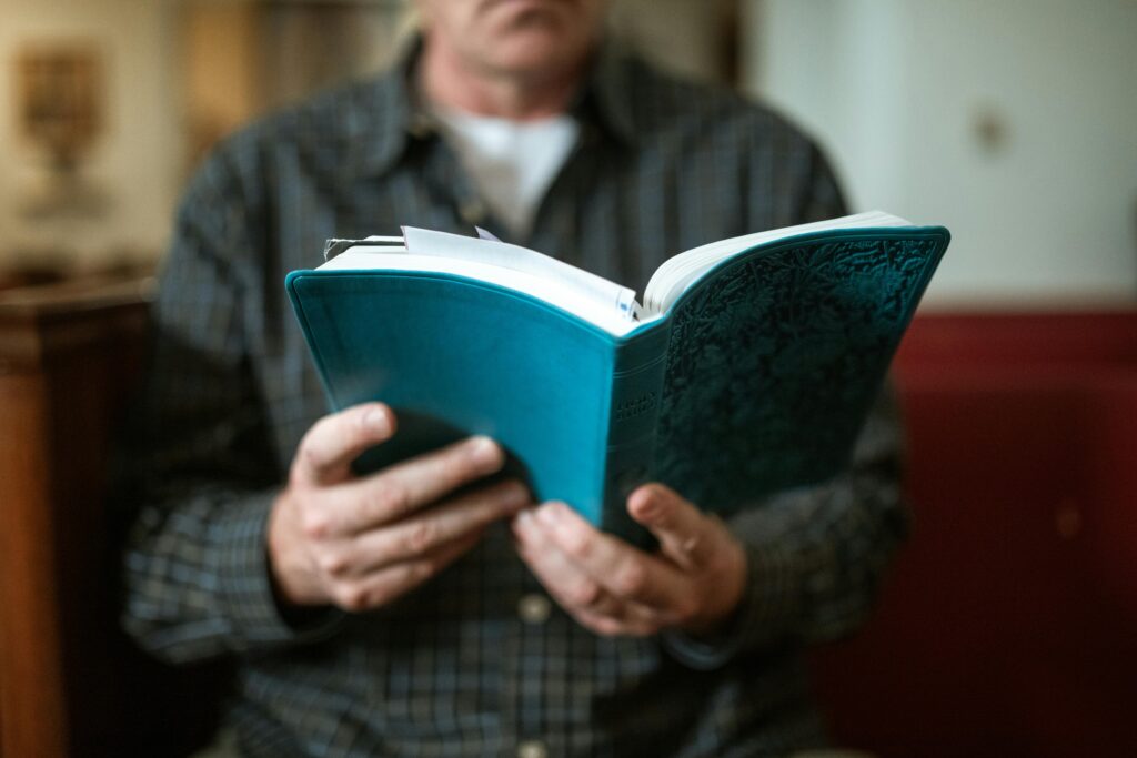 Adult man holding and reading a religious book inside a church.
